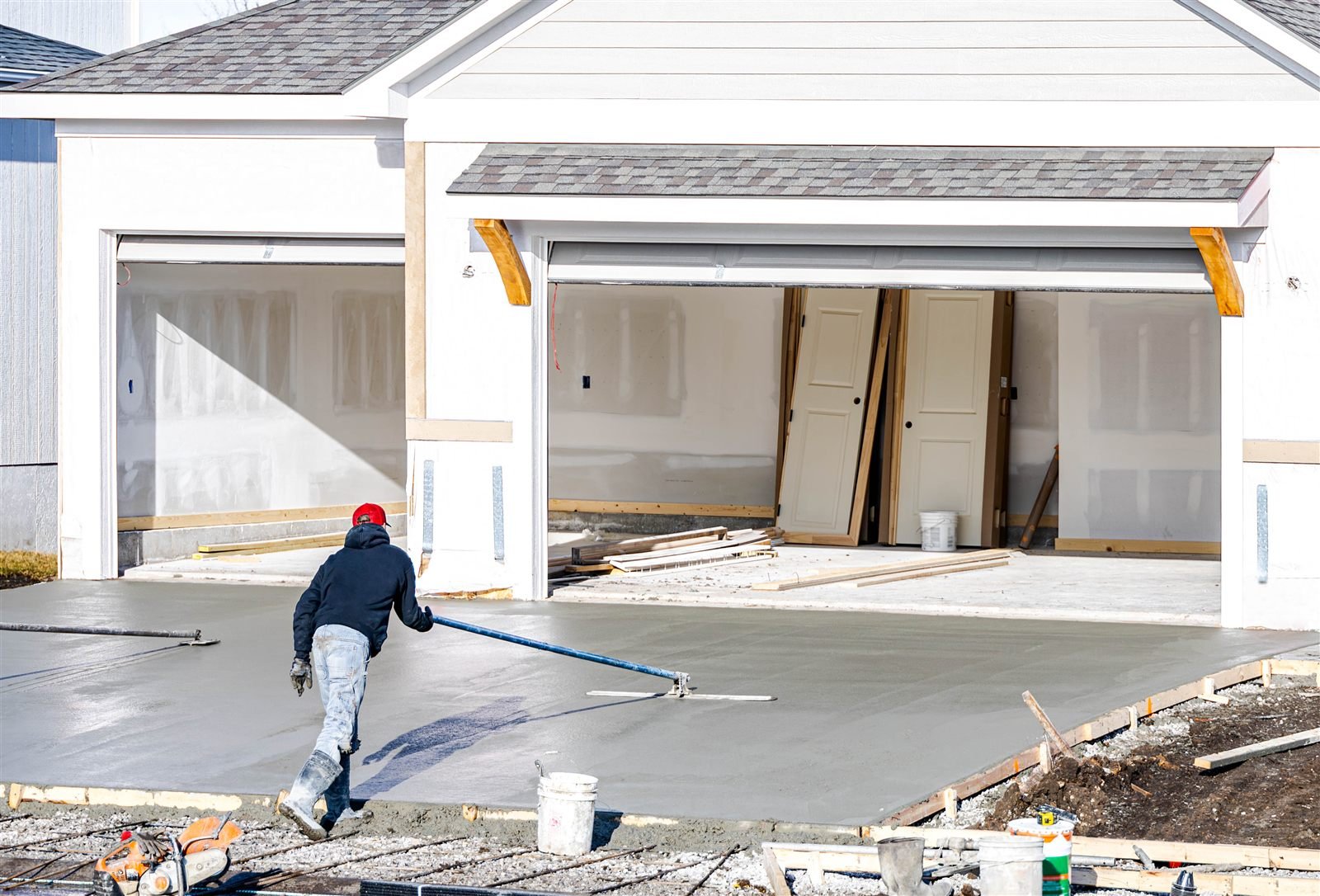 Worker bull-floating a fresh concrete driveway in front of a garage in Omaha, NE